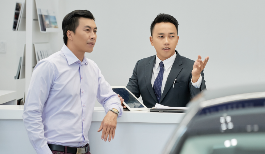 A Salesman talking to a customer in a dealership holding a tablet