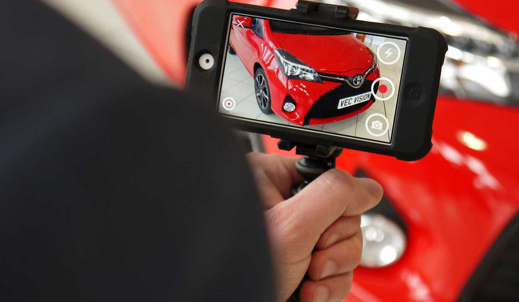 Close up of person holding a mobile phone taking imagery of the front of a red vehicle