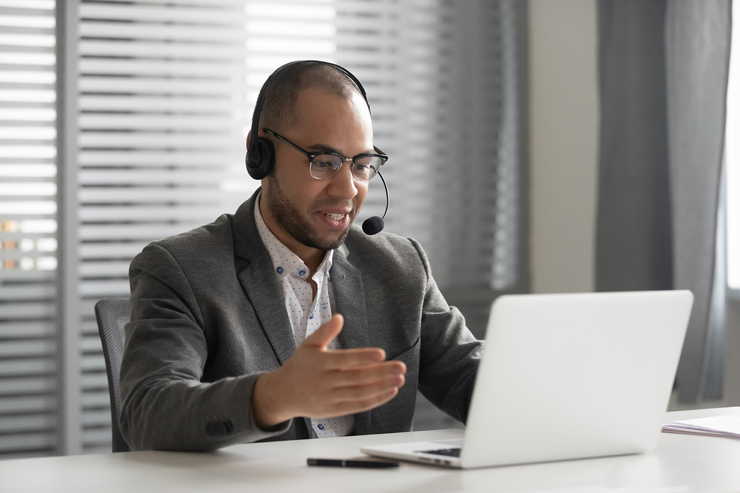 Smiling African American employee in headset using laptop, talking, call center operator agent in headphones with microphone consulting client customer, student learning language online